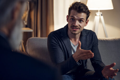 Man talking with intensity during a serious conversation, possibly in a therapy session, highlighting the impact of verbal conflict or emotional expression.