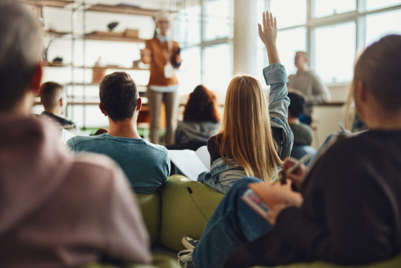 Student raising their hand in a classroom setting, representing engagement, learning differences, and the importance of support for autistic individuals in educational and mental health environments.