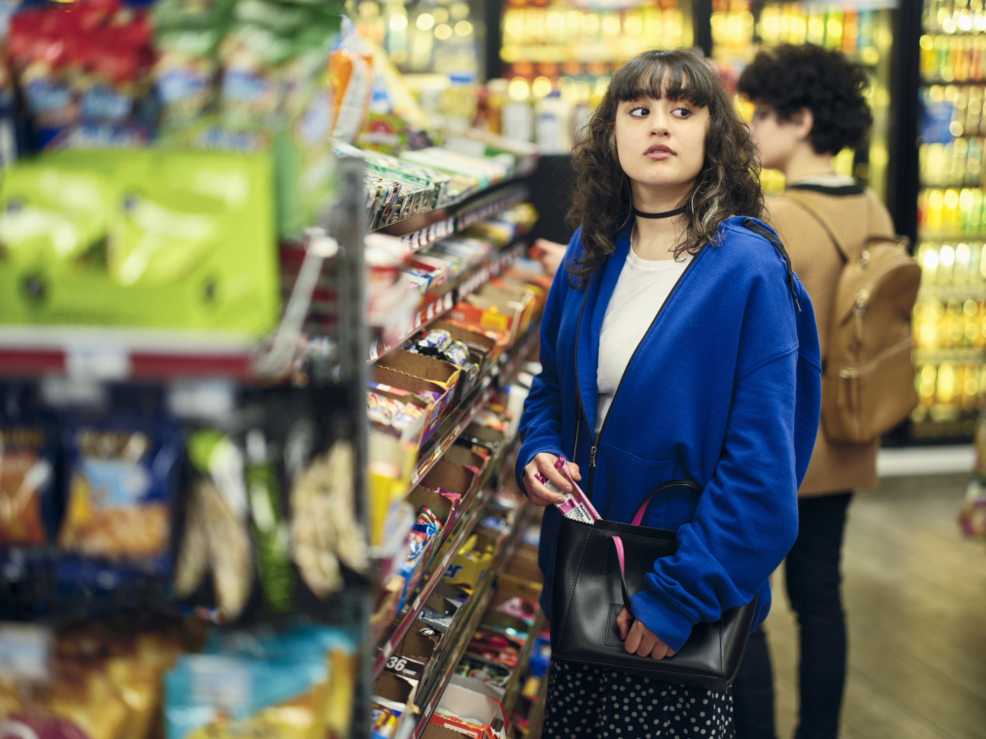 Teen girl in a convenience store glancing sideways while holding an item, suggesting secrecy or hesitation—illustrating behaviors associated with stealing or kleptomania.