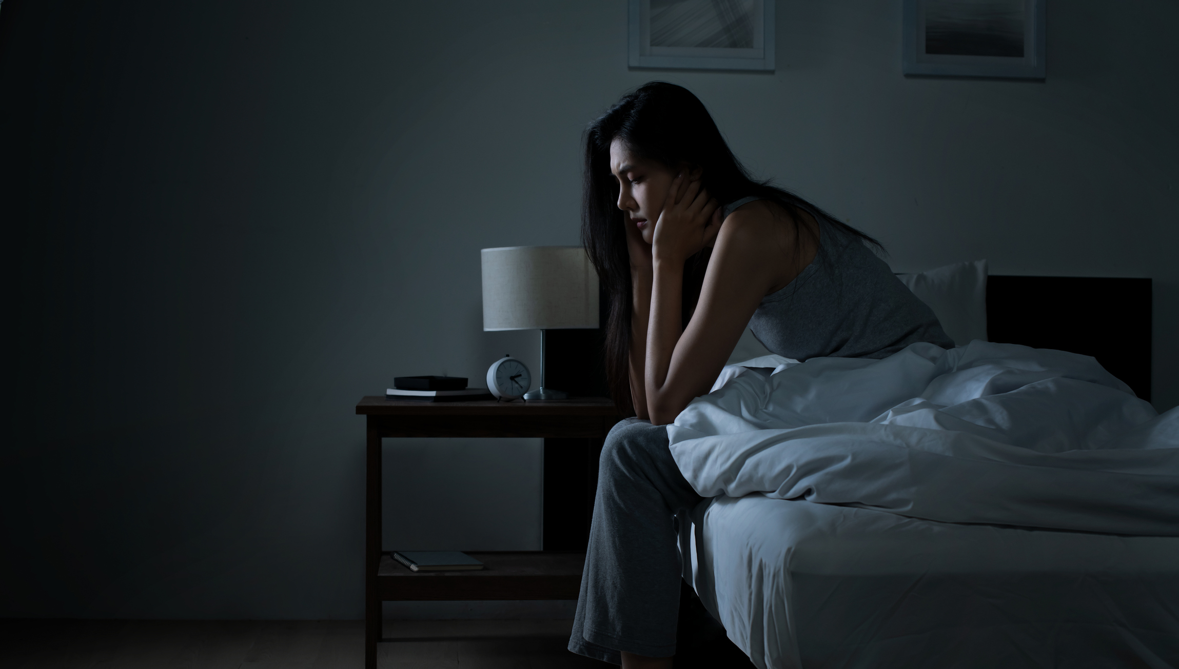 Woman sitting on the edge of a bed in a dark room with her head resting on her hand, conveying sadness, loneliness, or emotional exhaustion—symbolizing the overlap between autism and depression.