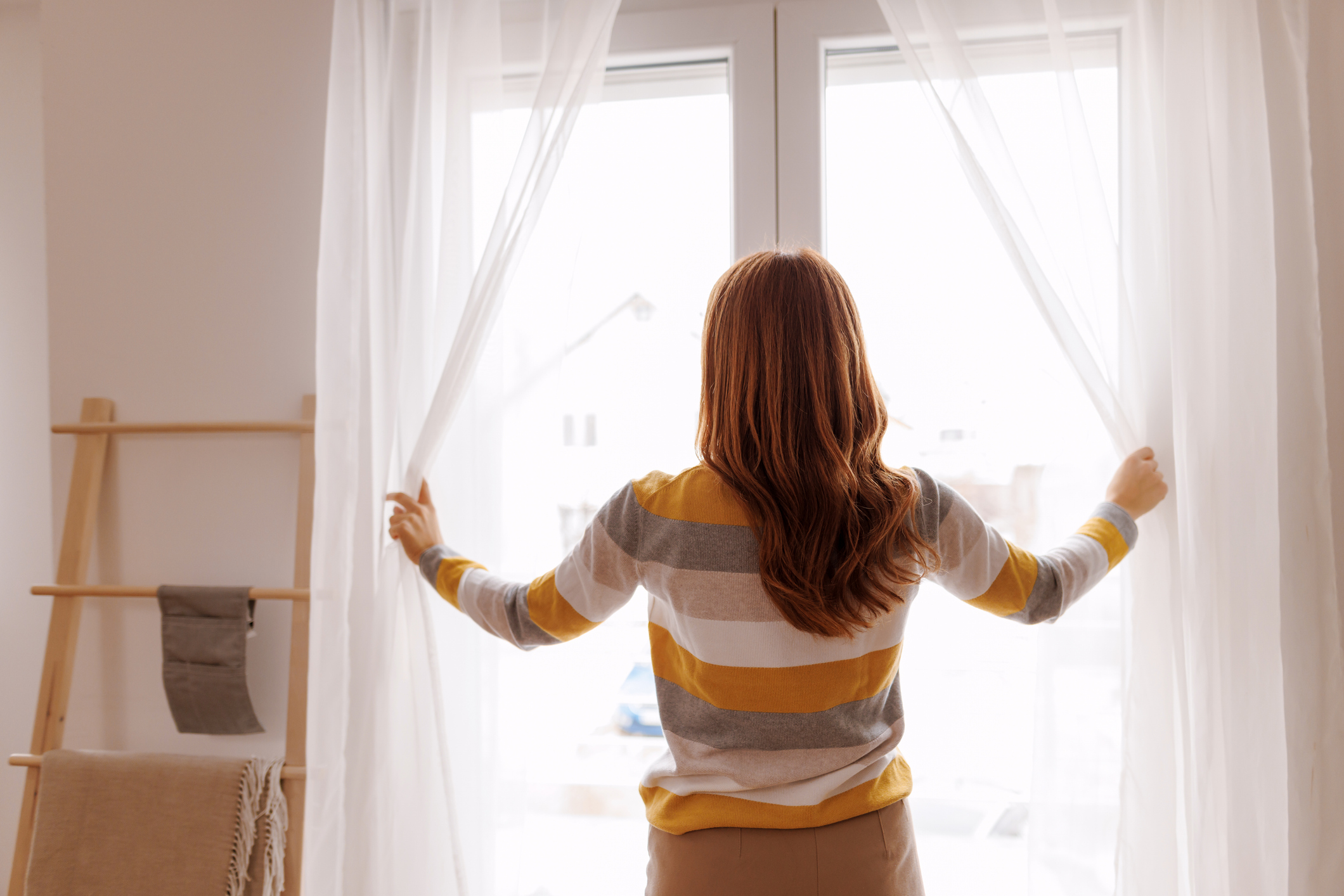 Young woman smiling and opening windows, symbolizing self-confidence, growth, and embracing new beginnings.