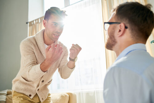 Man gesturing aggressively and speaking intensely to another man, possibly portraying grandiosity or a confrontational delusional episode.