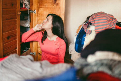 Young woman sitting in a cluttered room, looking overwhelmed while organizing clothes—depicting executive functioning challenges linked to ADHD.