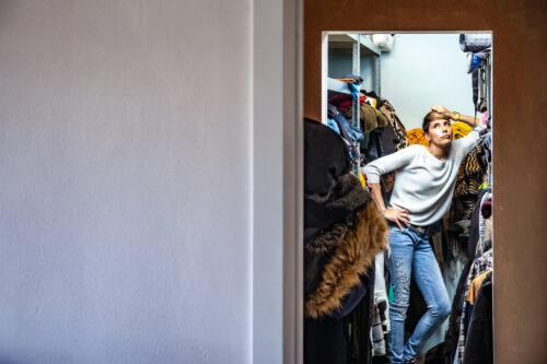 Woman standing in an overstuffed closet, appearing overwhelmed by clutter, illustrating a moderate level of hoarding behavior.