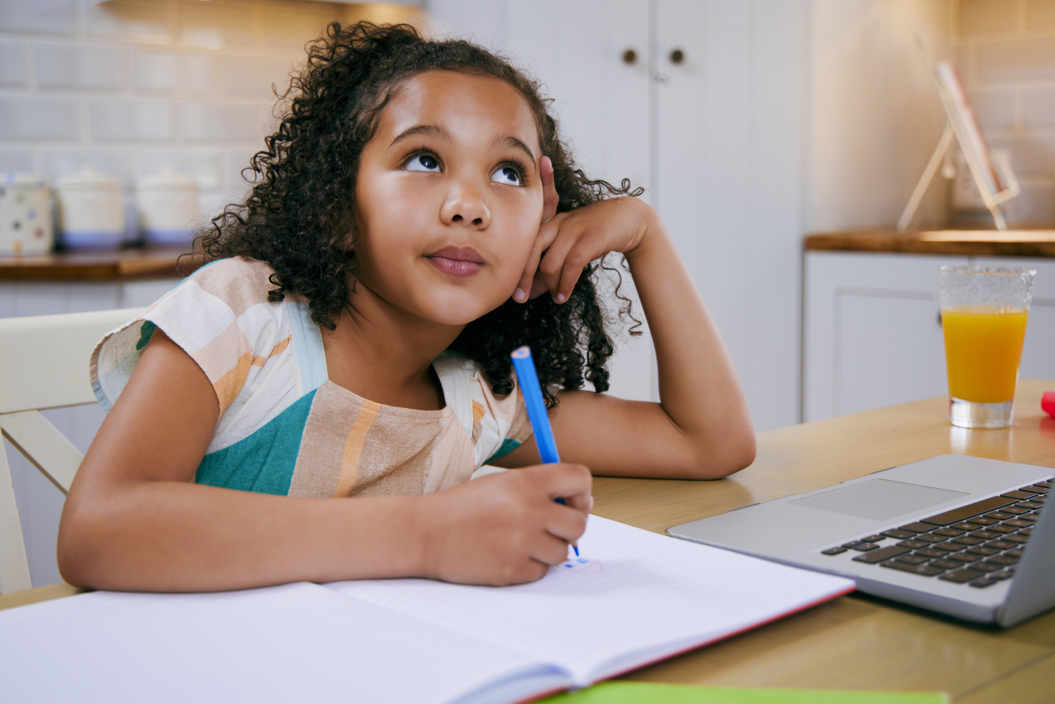 Young girl staring off in thought while holding a pen, representing the daydreaming and distractibility common in children with inattentive ADHD.