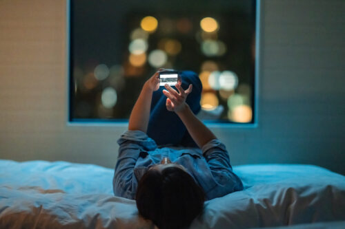Person lying in bed at night scrolling on their phone, representing rumination and difficulty disconnecting—common traits in individuals with high levels of neuroticism.