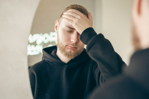 Man holding his forehead with eyes closed, appearing overwhelmed or distressed, possibly experiencing an emotional trigger.