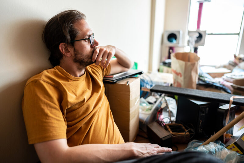 Man sitting in a cluttered room, deep in thought, representing internal compartmentalization in the midst of external chaos.