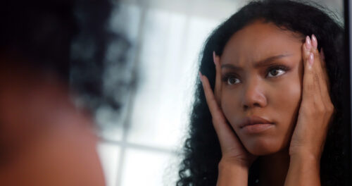 Young woman looking at herself in the mirror with a distressed expression, capturing the emotional intensity and self-reflection often experienced with PMDD.