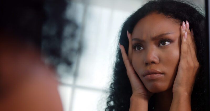 Young woman looking at herself in the mirror with a distressed expression, capturing the emotional intensity and self-reflection often experienced with PMDD.