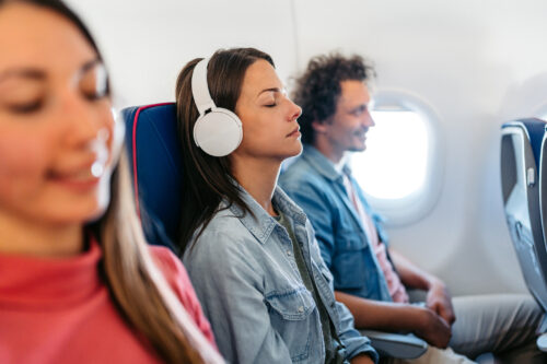 Woman wearing headphones with eyes closed on a plane, appearing relaxed—suggesting the calming effects of flight anxiety medication.