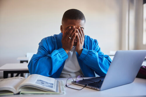 Teen boy holding his head in frustration while studying, showing signs of inattention or overwhelm often explored in ADHD screenings.