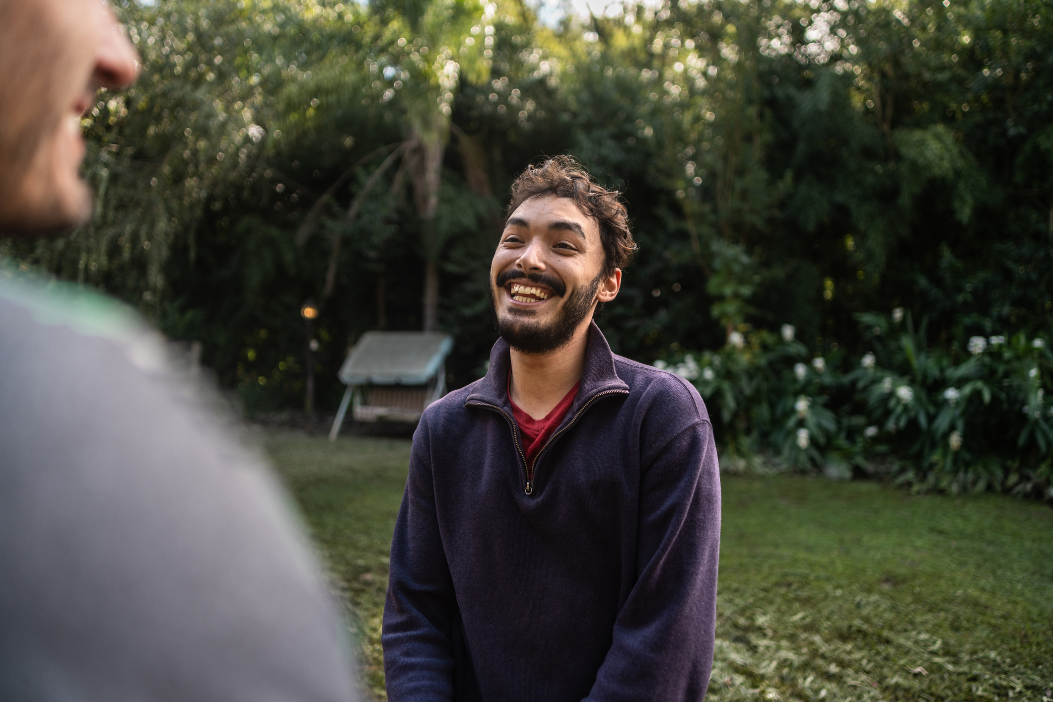 Young man smiling with confidence in a garden, representing growth in self-worth after overcoming feelings of inferiority.