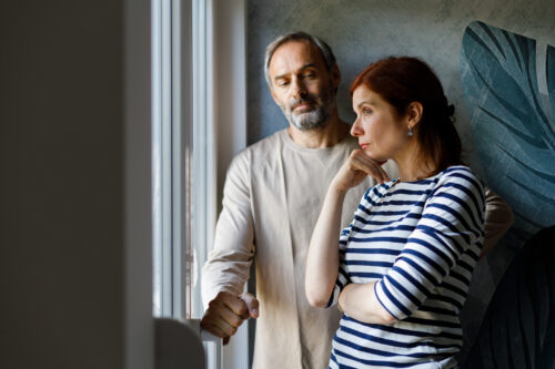 Man and woman standing tensely by a window, representing emotional manipulation and confusion often experienced in narcissistic gaslighting.