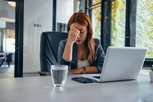 Stressed woman sitting at a desk with her hand on her forehead, reflecting the difficulties in focus and organization that can arise from executive functioning challenges.