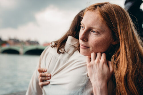 Woman hugging her partner tightly while looking away with a pensive expression, symbolizing emotional vulnerability and anxiety in relationships.