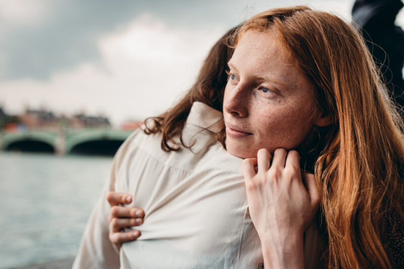 Woman hugging her partner tightly while looking away with a pensive expression, symbolizing emotional vulnerability and anxiety in relationships.