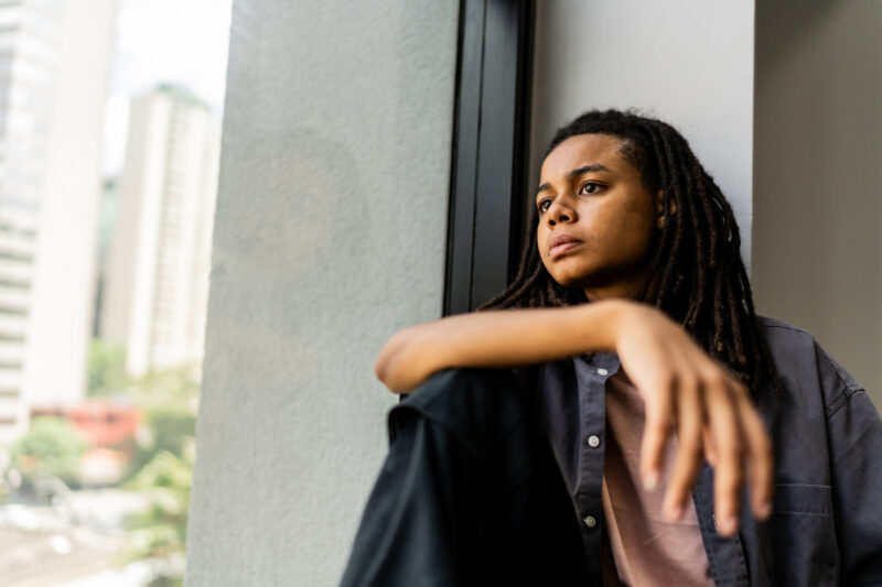 Teen staring out a window with a distant expression, representing the confusion and detachment that can accompany hallucinations.