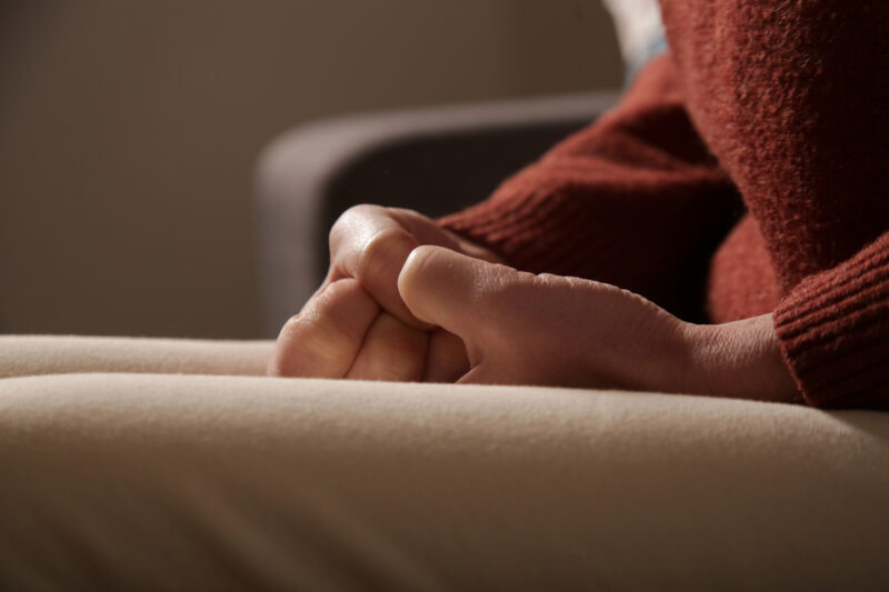 Close-up of a person sitting with hands tightly clasped in their lap, showing physical tension and anxiety often associated with high neuroticism.