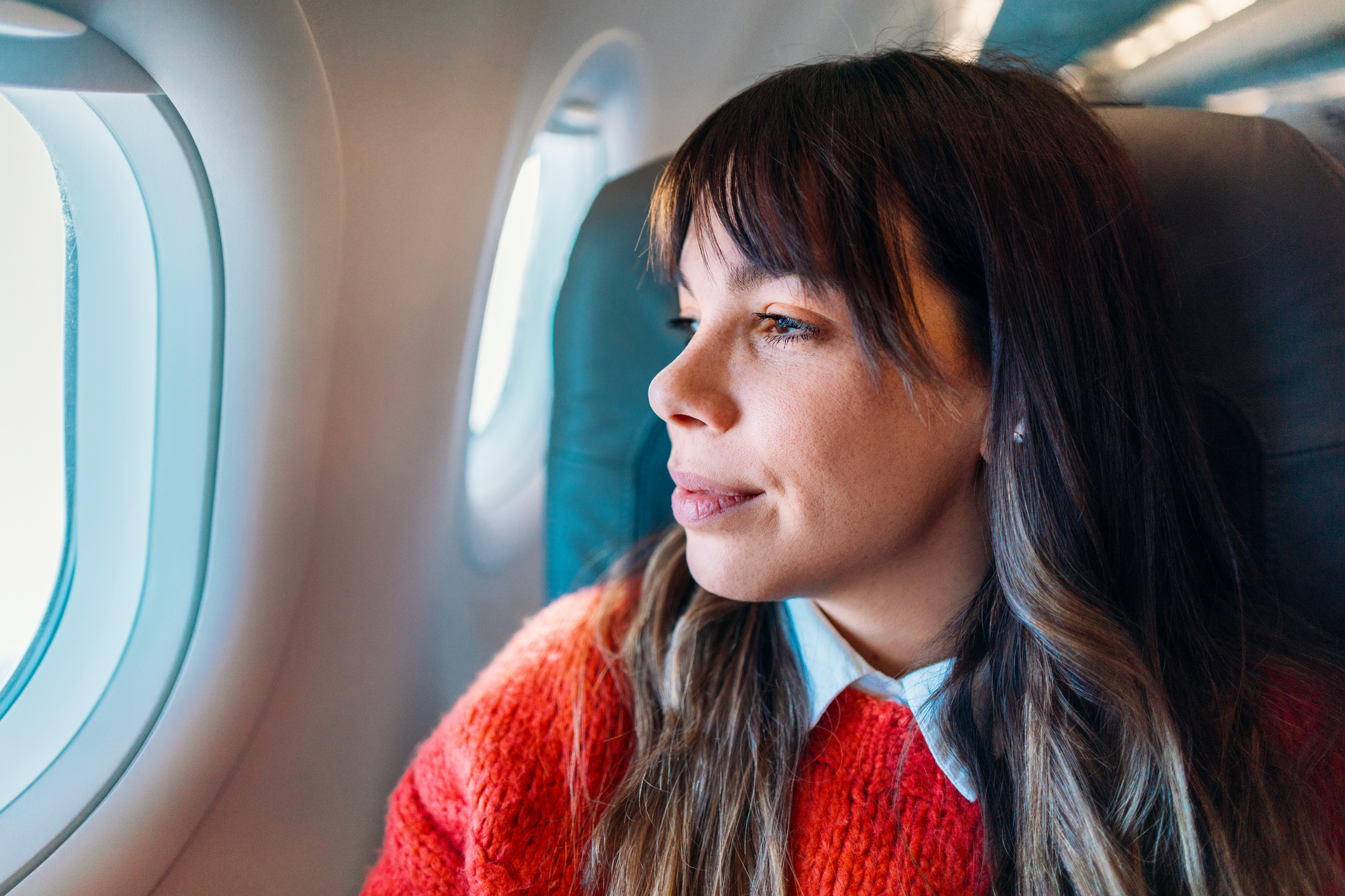 Woman sitting on a plane looking out the window calmly, representing someone working through a fear of flying.