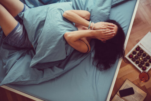 Woman lying in bed with hands over her face, showing signs of emotional distress that could indicate PMDD or severe PMS symptoms.
