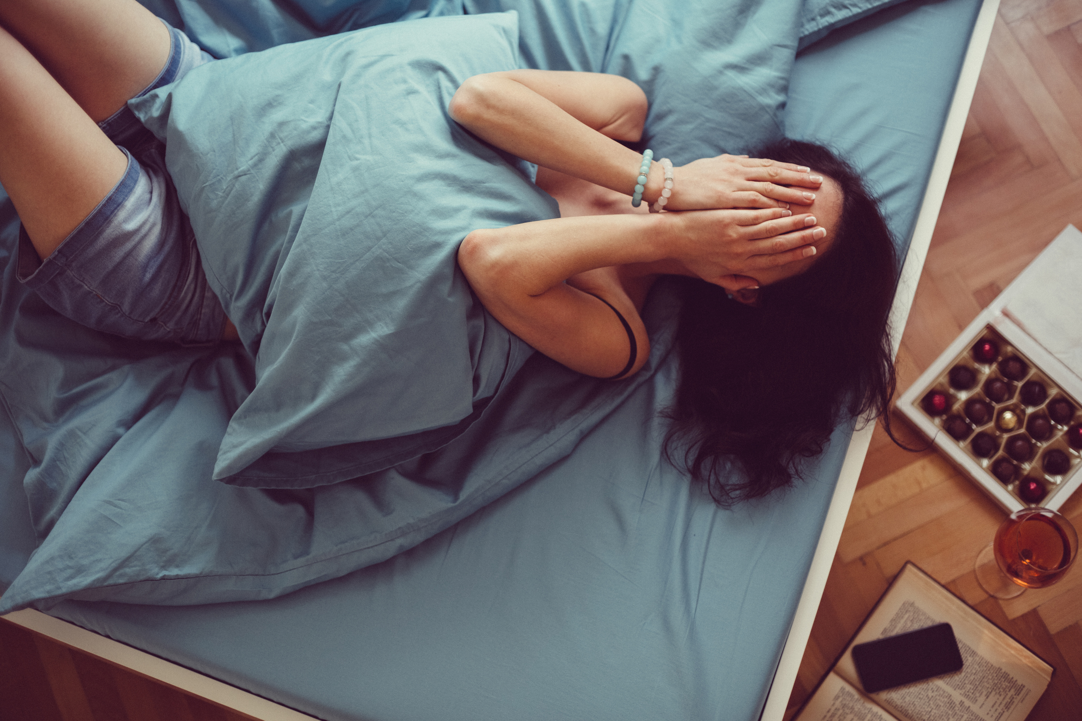 Woman lying in bed with hands over her face, showing signs of emotional distress that could indicate PMDD or severe PMS symptoms.