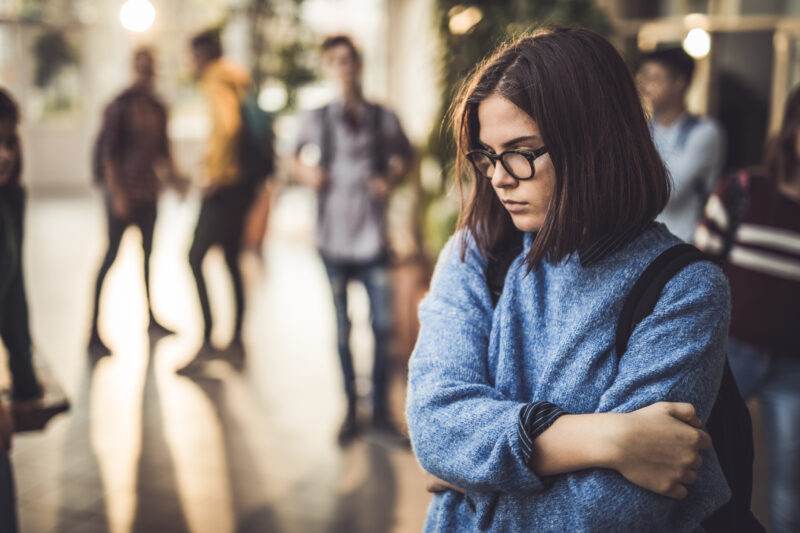Young woman in glasses looking down, reflecting the emotional weight of mental health stigma.