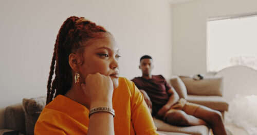 Woman looking away thoughtfully with partner in background, illustrating emotional distance and relationship burnout.