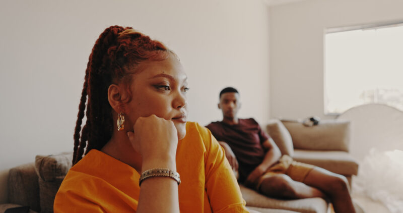Woman looking away thoughtfully with partner in background, illustrating emotional distance and relationship burnout.
