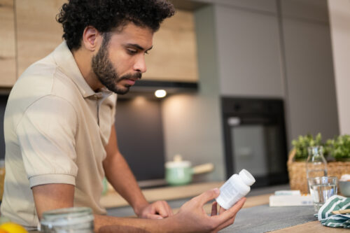 Man reading a medication bottle at home, representing careful consideration of Naltrexone for Alcohol Use Disorder treatment.