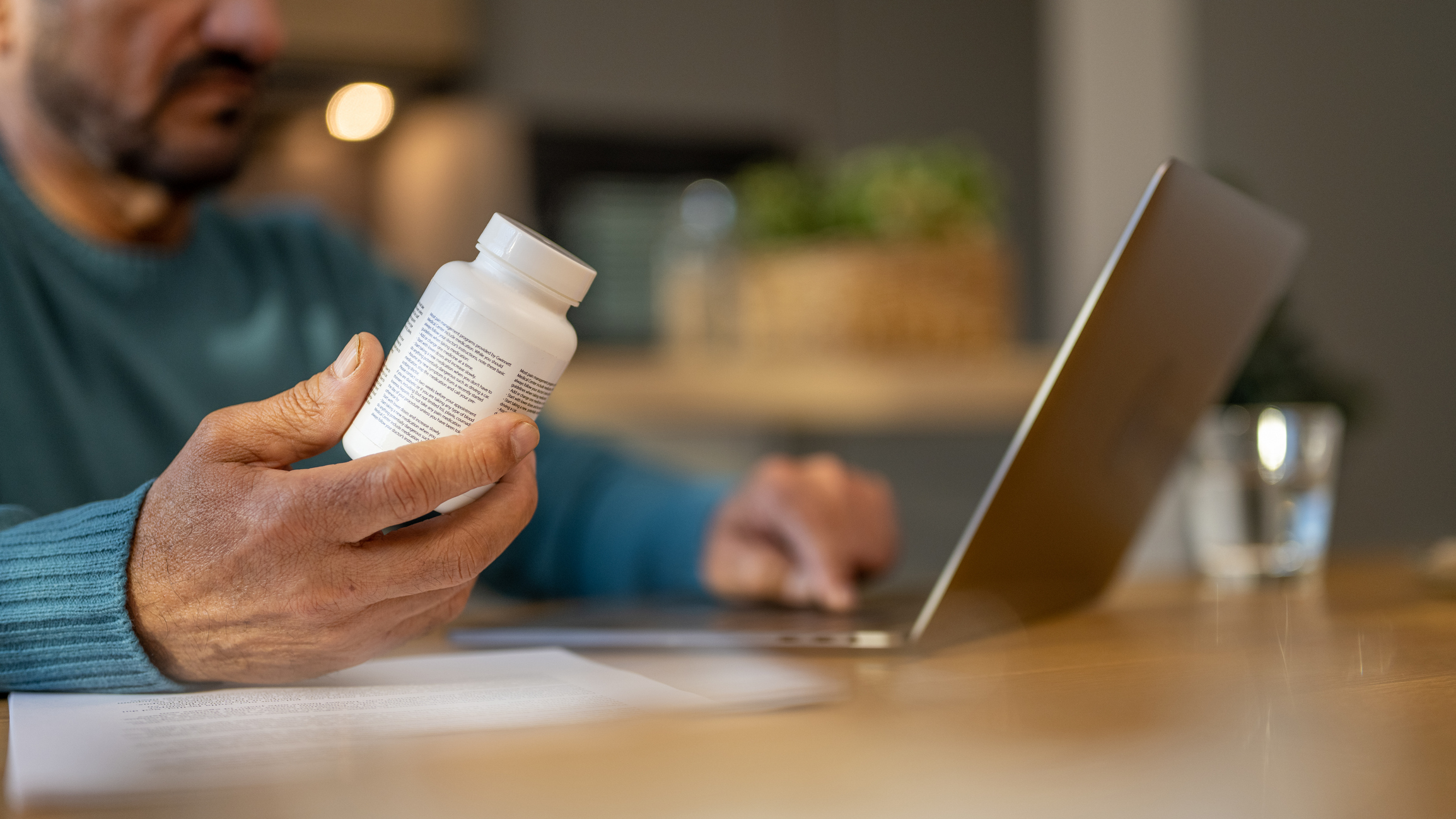 Man examining a medication bottle while researching online, representing caution and education around low dose Naltrexone.