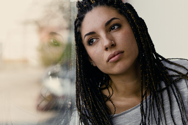 Woman looking out window thoughtfully, representing the complex connection between trauma and schizophrenia.