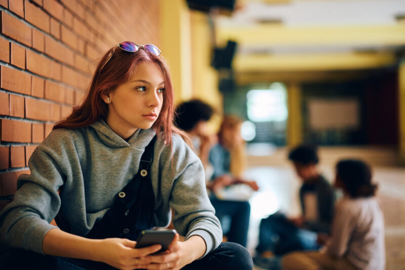 Teen girl sitting alone, looking away pensively, reflecting the mindset and isolation of victim mentality.