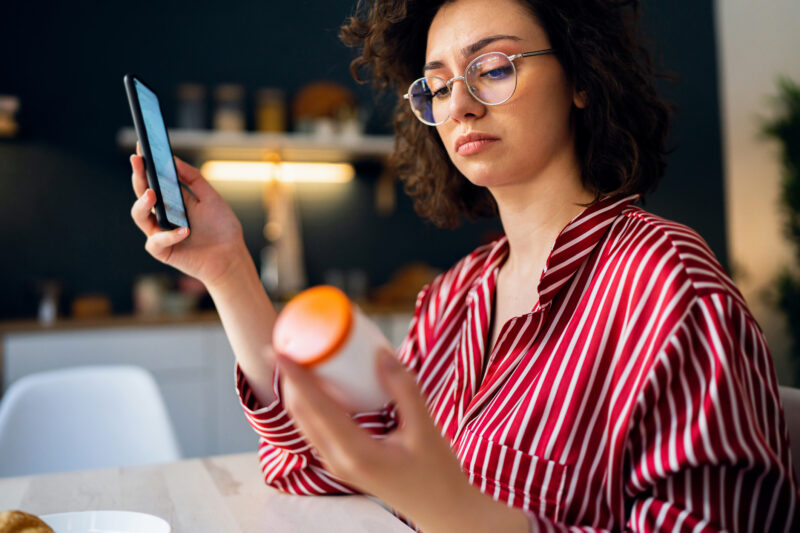 Woman examining pill bottle and phone, symbolizing concern about Suboxone use and its potential for dependence.