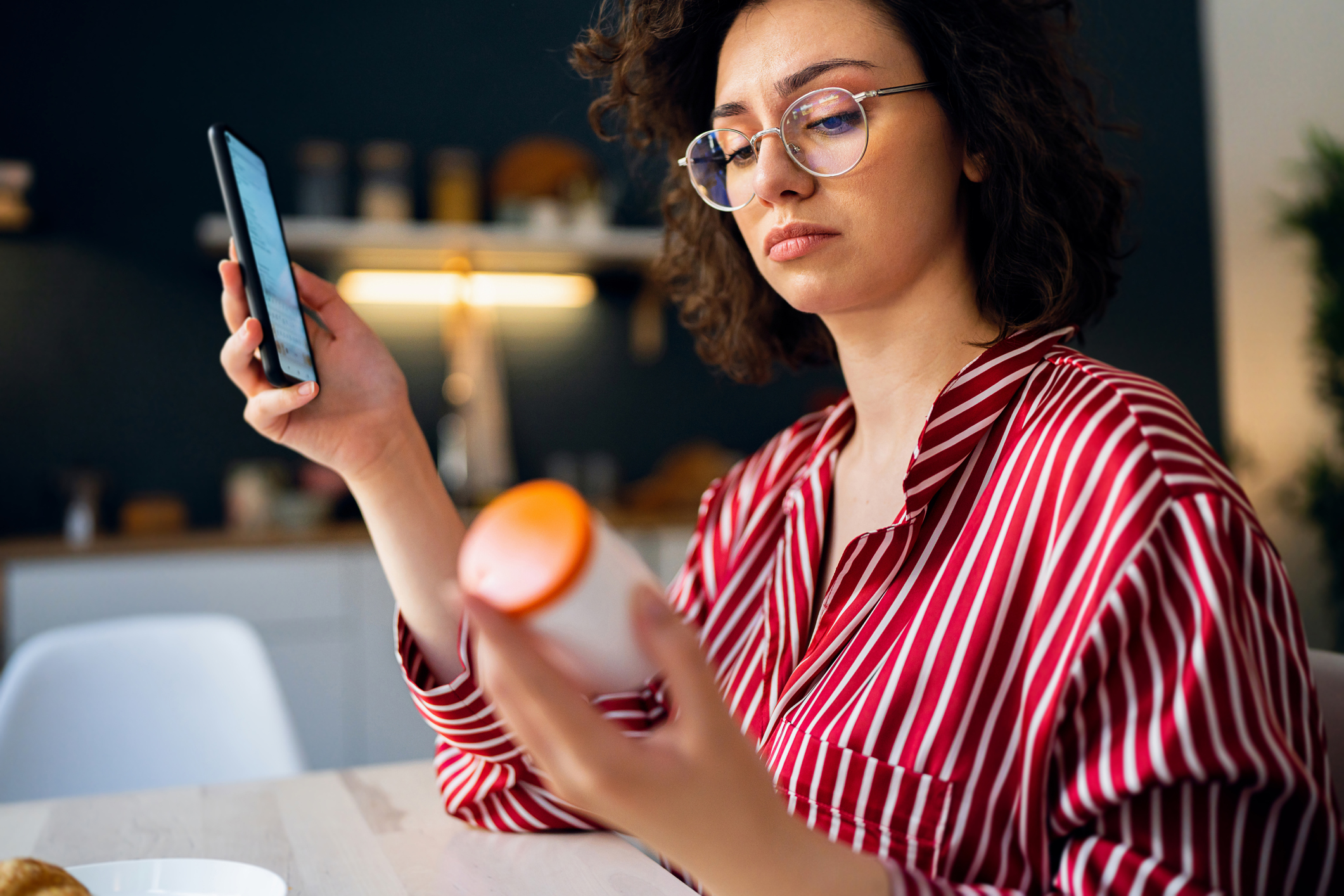Woman examining pill bottle and phone, symbolizing concern about Suboxone use and its potential for dependence.