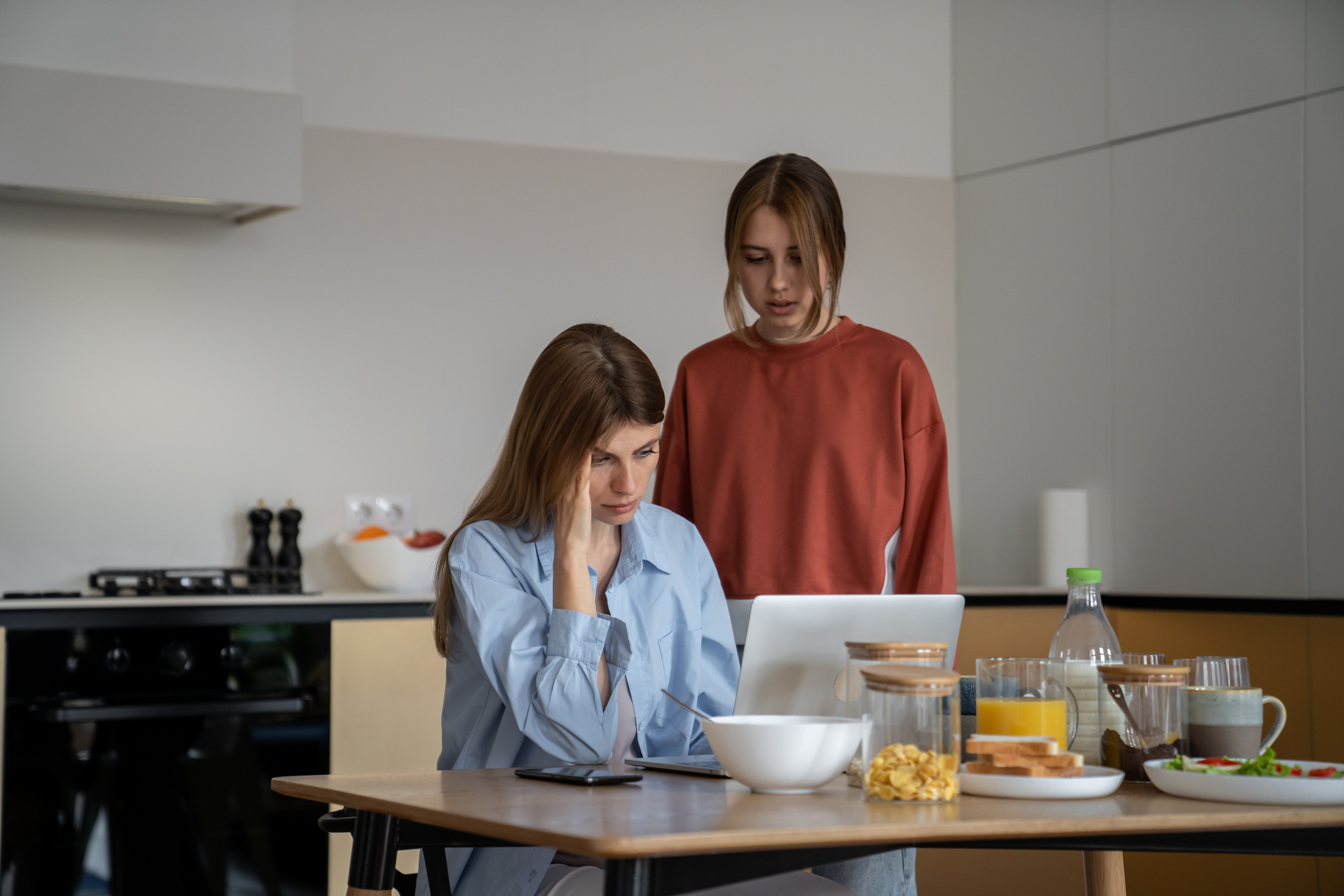 Worried young woman comforting her stressed friend at the kitchen table during breakfast.