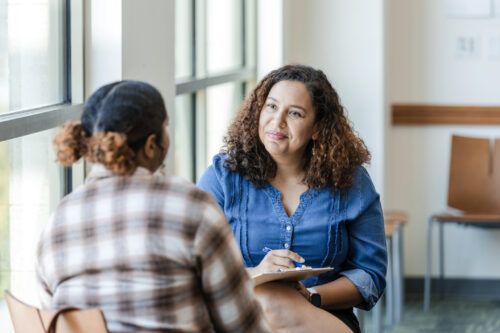 Unrecognizable female university student shares struggles with female therapist who is practicing person-centered therapy.