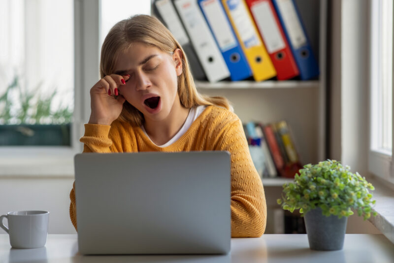 Woman yawning at laptop, illustrating how fatigue or frequent yawning can sometimes relate to anxiety symptoms.