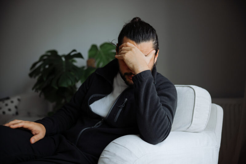 Man sitting with head in hand, illustrating emotional distress linked to mania or psychosis.