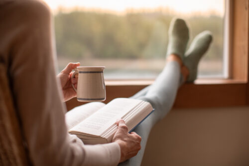 Person relaxing with a book and mug, practicing self-care to cope with life’s difficult moments.