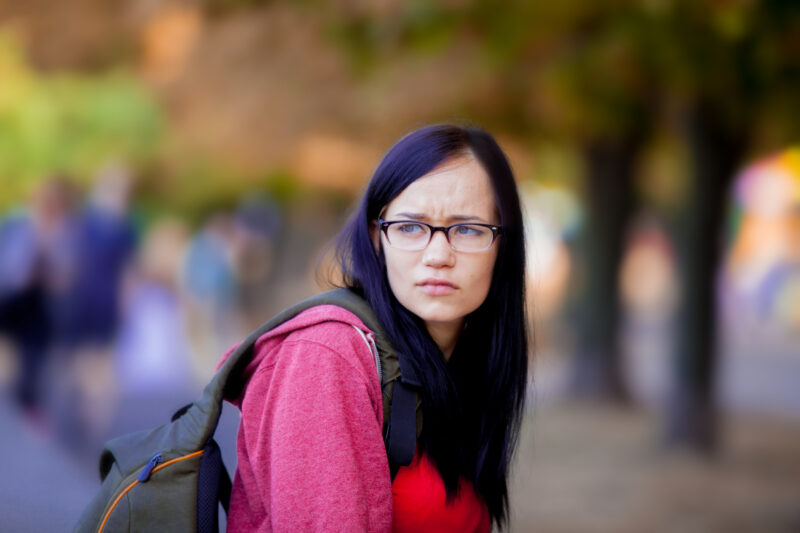 Young woman with glasses looking upset, reflecting feelings of frustration, doubt, and self-loathing.