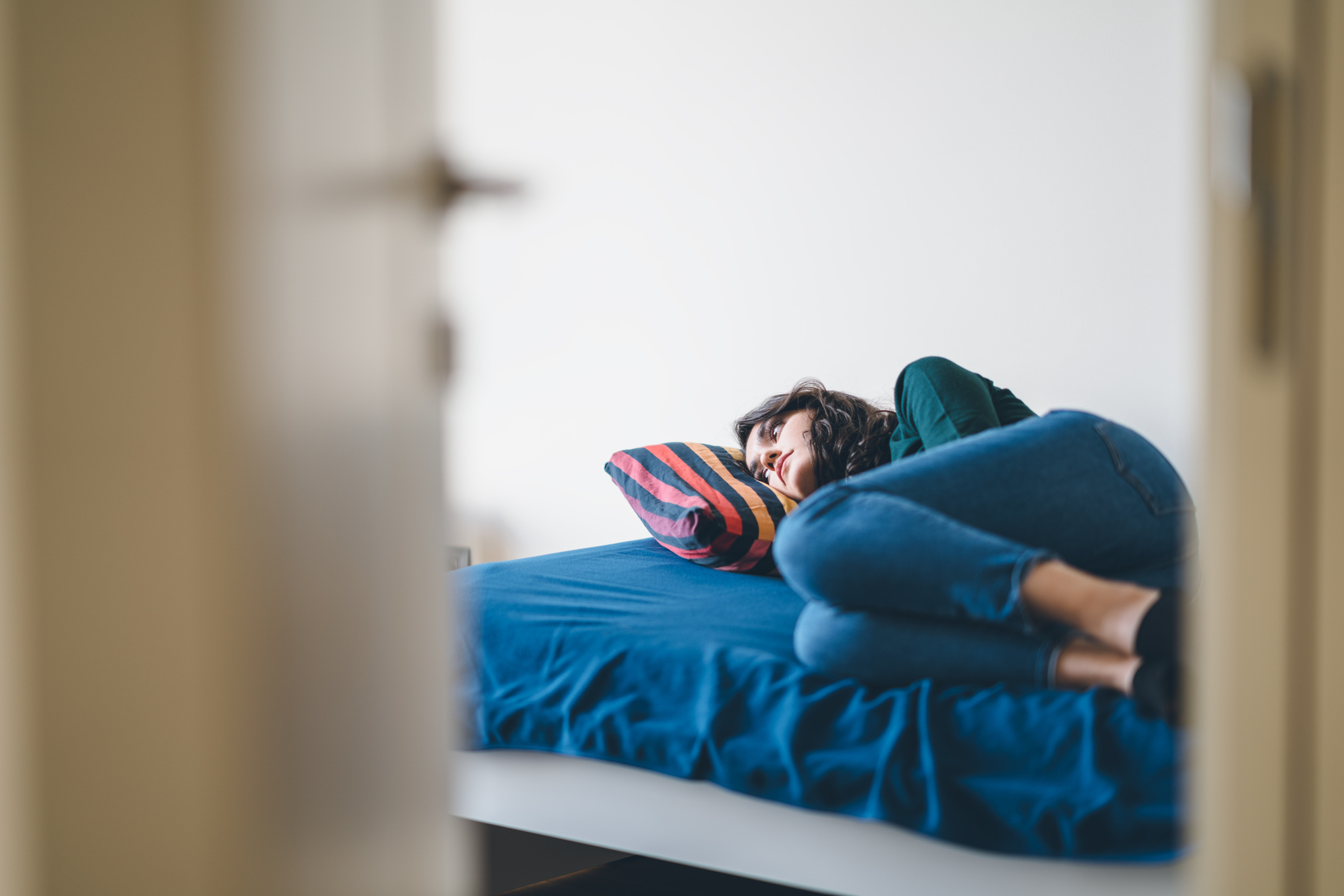 Person lying curled up on a bed, looking away with a distant expression, reflecting emotional distress or withdrawal often associated with eating disorders.