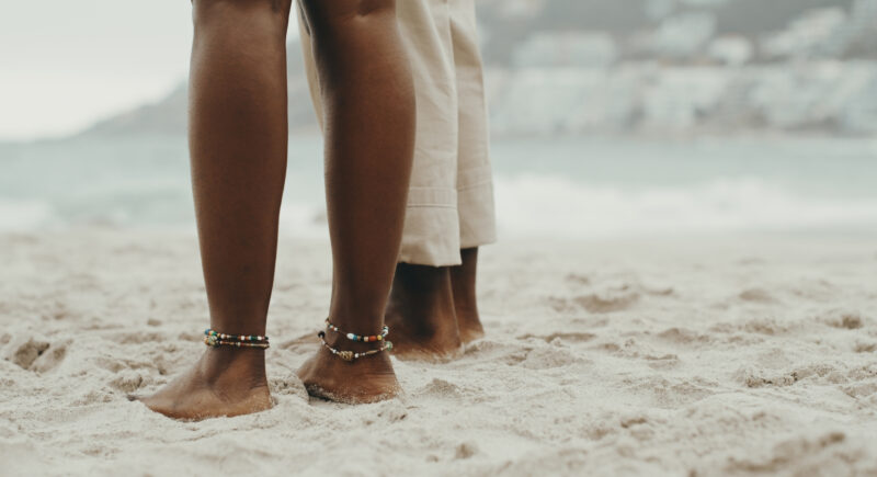 Close-up of sandy feet with painted toenails on a beach, symbolizing summer body pressure, beauty standards, and body image challenges during warm-weather months.