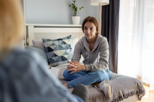 Teen girl sitting cross-legged on a bed during a therapy session, representing the importance of early intervention and talk therapy in anorexia treatment.