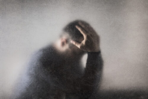 Blurry image of a man holding his head in distress, conveying intense emotional pain or mental fog commonly associated with major depressive episodes.