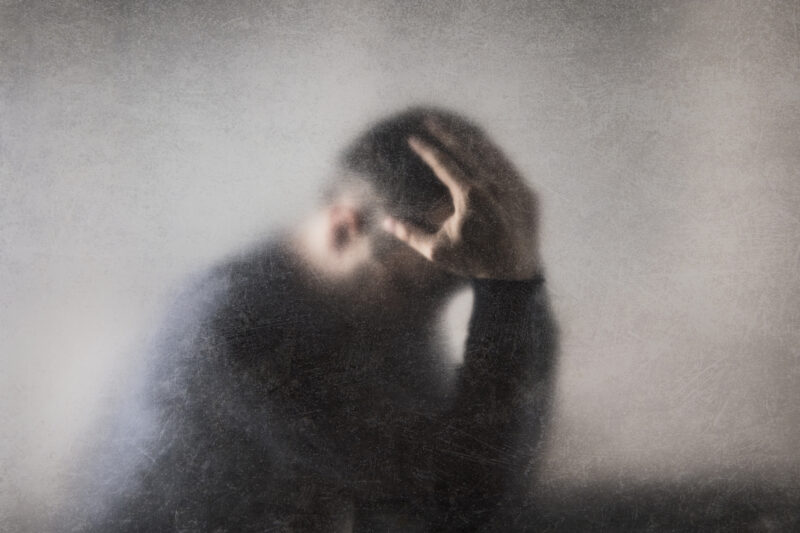 Blurry image of a man holding his head in distress, conveying intense emotional pain or mental fog commonly associated with major depressive episodes.