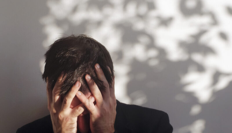 Man holding his head in both hands, face obscured by stress or overwhelm, representing the cognitive and emotional overload often associated with ADHD.