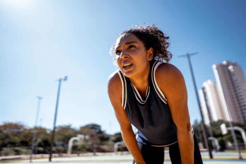 Woman sweating and catching her breath under intense sun, illustrating the mental and physical strain of extreme heat and its impact on emotional well-being.