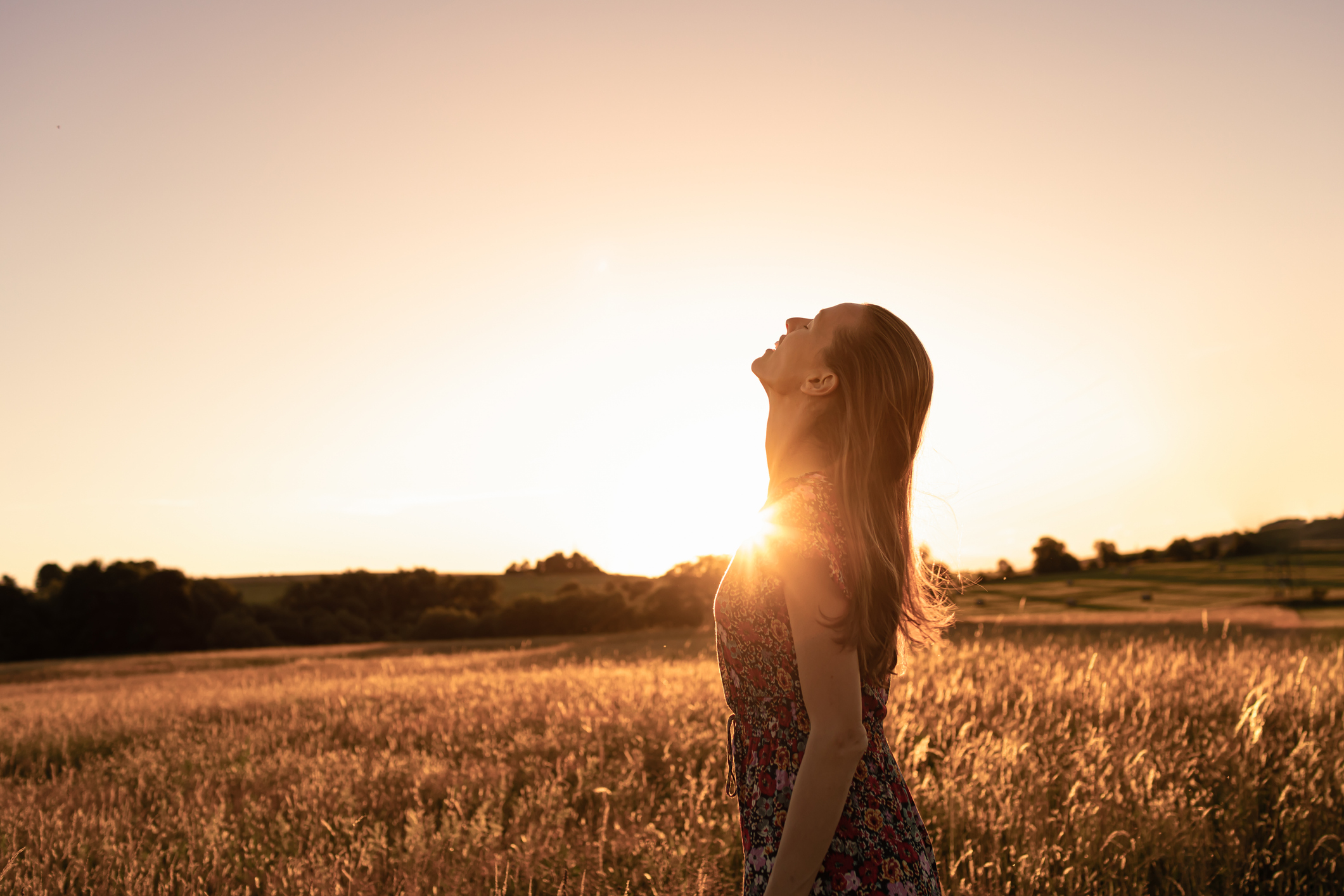 Woman standing in a golden field at sunset with head tilted back, symbolizing freedom, recovery, and the emotional healing process in anorexia treatment.