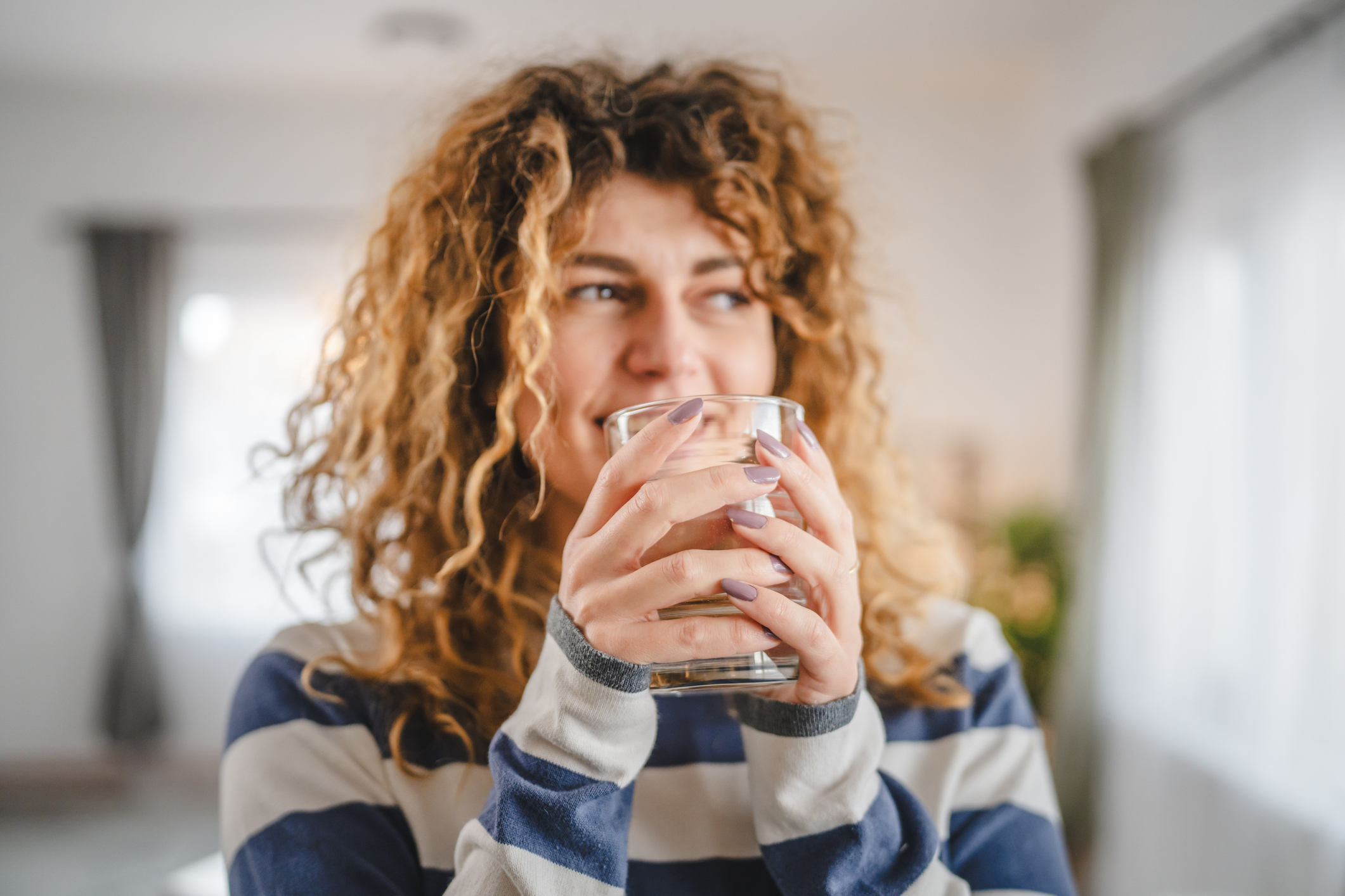 Woman holding a glass and smiling in a calm setting, representing comfort and the early stages of relief during Suboxone treatment for opioid use disorder.